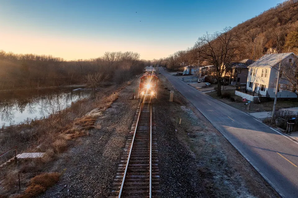 A train travels along tracks by a river in Reads Landing, MN, during sunset showcasing serene landscapes.
